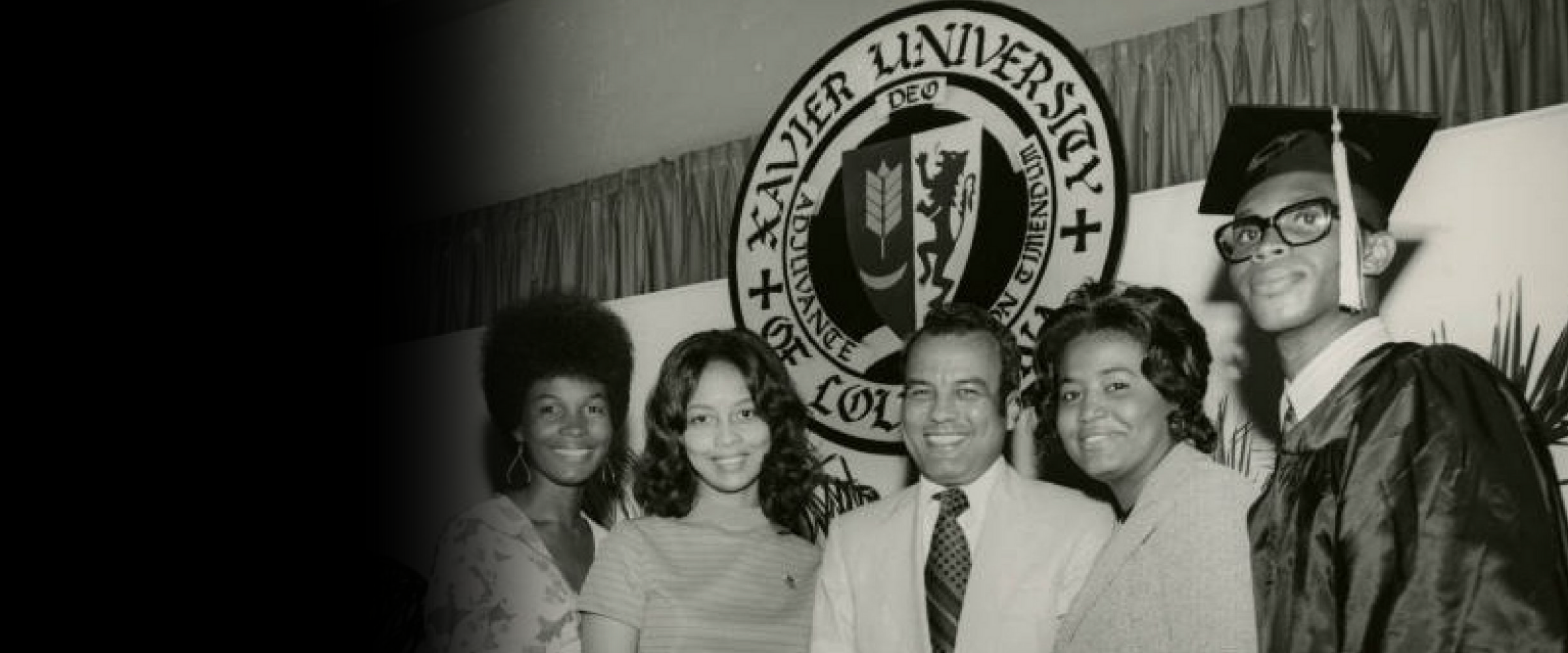 Former Xavier President Norman C. Francis with three female students and a male student who is in a graduation cap and gown.