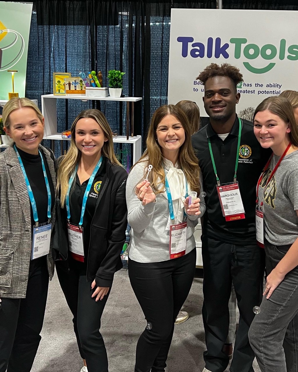 Graduate students and alumni stopped for a picture in the TalkTools booth at the 2022 ASHA Convention.