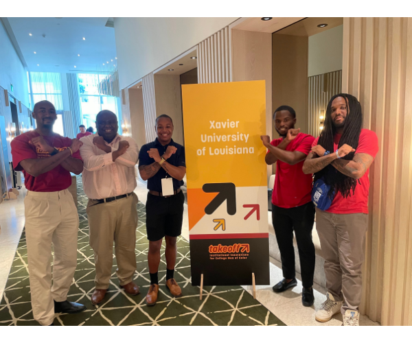 Five men standing next to a banner that says "Xavier University of Louisiana", holding up X's with their arms