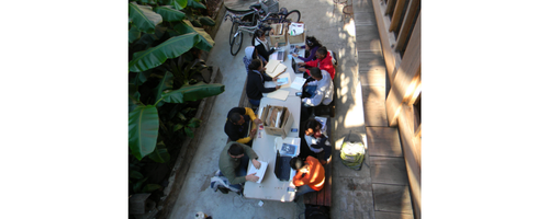 Overhead view of nine people working at a table spread with papers, folders, and cardboard boxes
