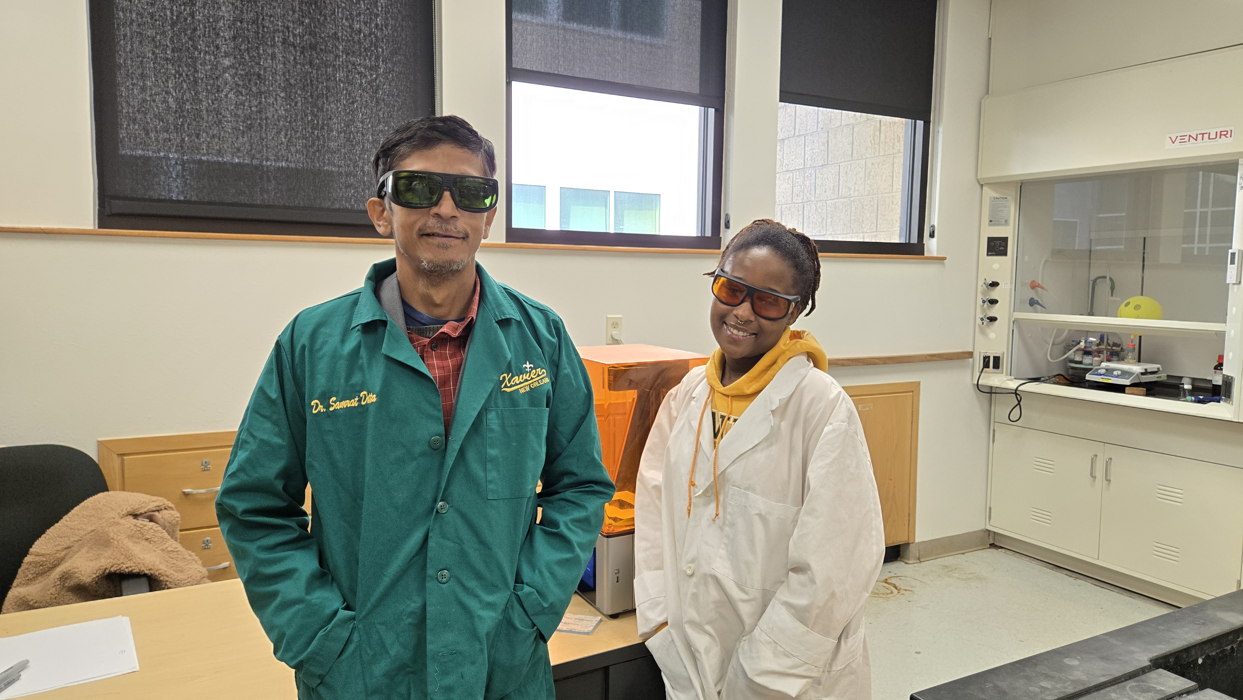 Olivia Downey (’26) on the right in a white lab coat with her research mentor, Dr. Samrat Dutta on the left in a green lab coat.