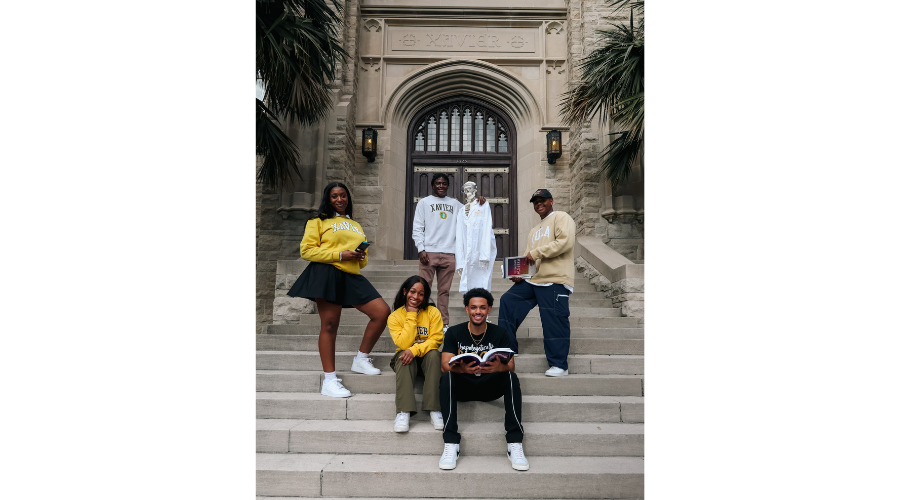 Five students standing outside on a staircase at Xavier University of Louisiana with a skeleton wearing a lab coat.