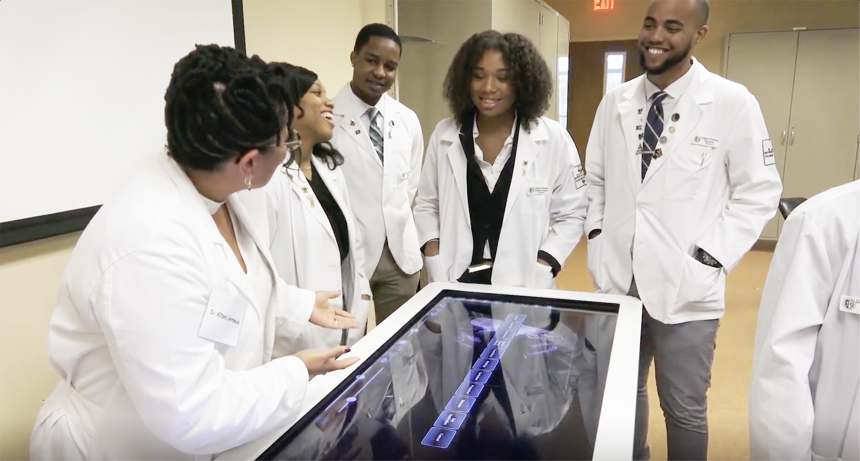 Students in white coats training at simulation table